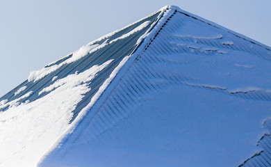 Snow on the roof of the house against the blue sky