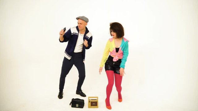 An old fashioned young man and a girl dancing. Man is holding a phone; purse and boombox are on the floor