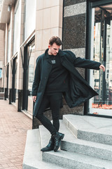 handsome stylish young man in a trendy vintage coat walks in the city