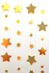A garland of golden stars strung on a thread. Vertical image. Designer background for decoration in the room. Christmas wall decoration.