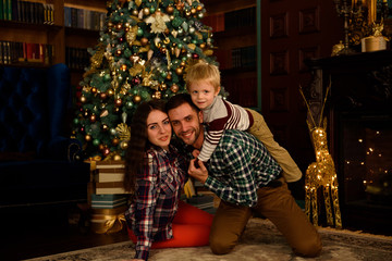 Naklejka na ściany i meble happy family mother father and baby at christmas tree at home