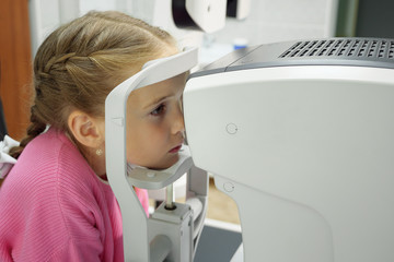 Optometrist examines the sight of little girl at eye clinic