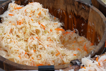 Fermented preserved vegetarian healthy food concept. Sauerkraut with orange carrots in wooden container is sold by weight in local market. - obrazy, fototapety, plakaty