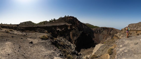 A woman with a backpack stands on the edge of the abyss and looks into the crater of a volcano. High resolution. © w1d
