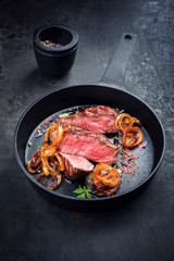 Modern Style classic dry aged sliced roast beef with fried onion rings served as closeup in a minimalistic design cast-iron skillet