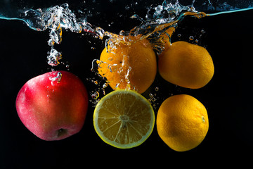 Various fruits clementine, lemon and apple splash of water on black