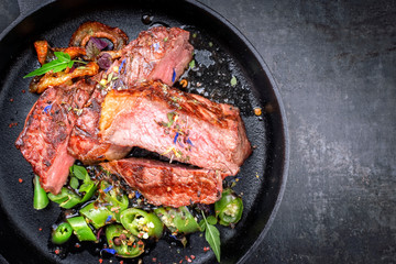 Modern Style classic dry aged sliced roast beef with fried onion rings and chili served as top view in a minimalistic design cast-iron skillet with copy space right