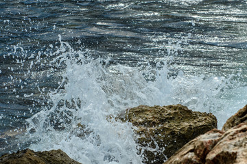 The foam of the surf on coastal rocks. The sea wave breaks from the stone.
