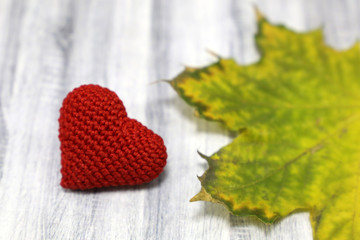 Red knitted heart and yellow maple leaf on wooden table. Background for health care in autumn season, depression, blood donation, love card