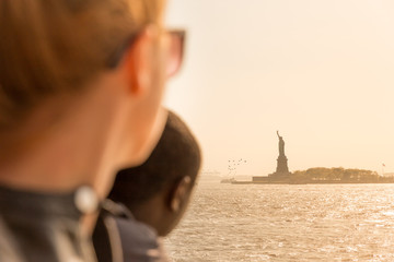 Tourists looking at Statue of Liberty silhouette in sunset from the staten island ferry, New York...