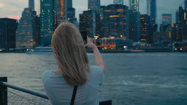 Attractive Caucasian female tourist taking pictures of New York City Manhattan downtown skyline with her smartphone. 4K UHD