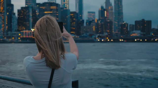 Attractive Caucasian female tourist taking pictures of New York City Manhattan downtown skyline with her smartphone. 4K UHD