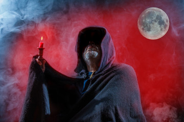 a scary man is standing with a candle in front of a red background with moon