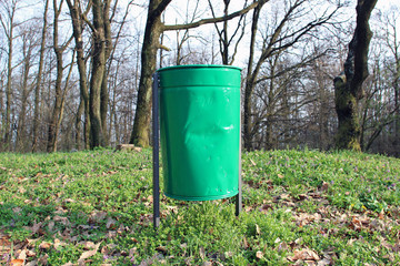 Demolished bent green metal garbage bin in park