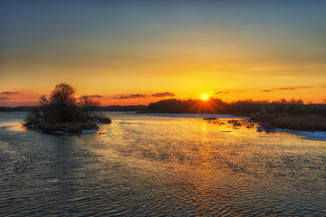 Obraz premium Beautiful russian early winter landscape with non frozen river, snow-covered riverside and small island at sunset. Scenic nature background