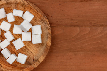 An overhead photo of sugar cubes on a wooden plate, shot from above on a dark rustic wooden background with copy space