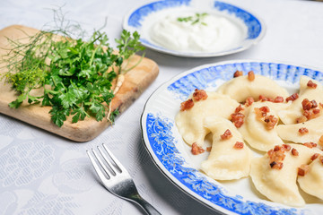 Traditional Polish dumplings with cheese and potatoes on a blue white plate. Next to cream and parsley on a wooden board.