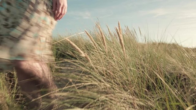 A woman in a summer dress walks toward the camera on beach dunes.