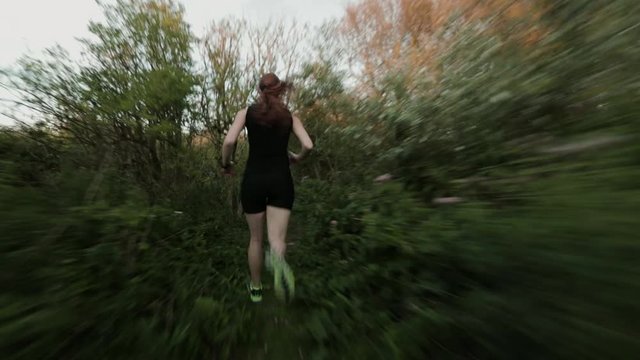 Tracking footage of an active and fit woman running outdoors on a narrow trail.