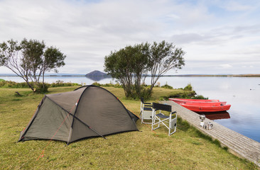Camping site with a tent, two folding chairs and boats at the coast of Myvatn lake, Iceland