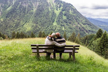 Couple sitting on a bench looking at the alpine landscape in the Allgau. Bavaria. Germany.