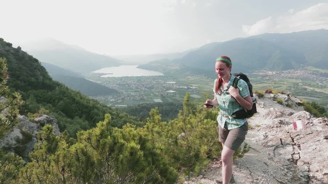 A female hiker navigates a scenic trail overlooking an Alpine lake in Italy.