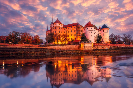 Wonderful sunrise view of Schloss Hartenfels, with colorful sky reflected in Elbe river . Picturesque morning view of castle on banks of the Elbe.  Torgau. Saxony, Germany. creative Scenic image