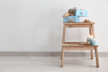 Wooden stand with burning candles and seashells near white wall