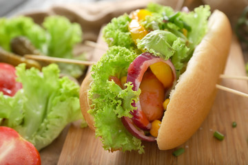 Tasty hot dog with vegetables on wooden board, closeup