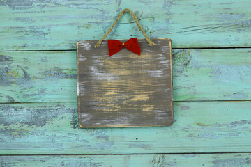 Blank wood sign with red Christmas bow hanging on antique rustic teal blue wooden door; holiday background with painted copy space
