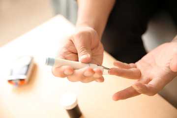 Diabetic man taking blood sample with lancet pen at home, closeup - obrazy, fototapety, plakaty