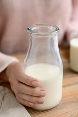 Woman with bottle of fresh milk at wooden table, closeup