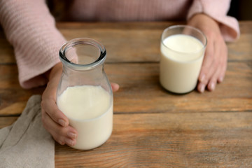 Woman with bottle and glass of fresh milk at wooden table