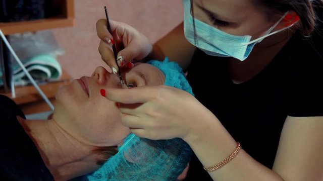 Makeup artist doing curling and keratin lash lift for female client, procedure for the care of eyelashes in a beauty salon, dolly shot.