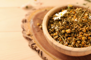 Wooden bowl with dried chamomile flowers on table, closeup