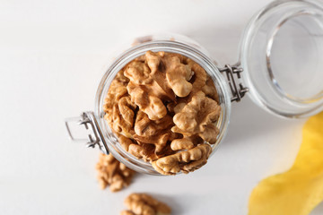 Glass jar with shelled walnuts on white table