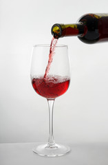 Pouring of tasty wine from bottle into glass on white background