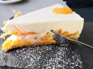 Mandarinenkuchen mit Mandarinenscheibe auf schwarzem Schiefer mit Puderzucker