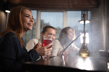 Three young women sitting in a cafe smoking hookah