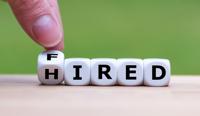 Hand is turning a dice and changes the word "fired" to "hired"