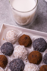 Chocolates with poppy seeds, coconut, nuts on a light background with a glass of milk.