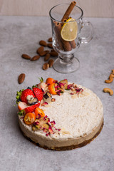 White cake with berries on the table with nuts, cinnamon, a glass, lemon.
