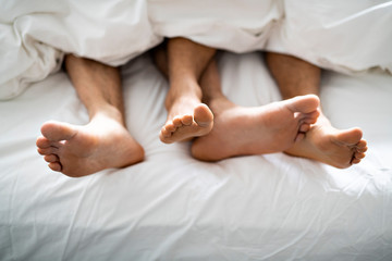two pairs of feet under duvet couple makes love in bed
