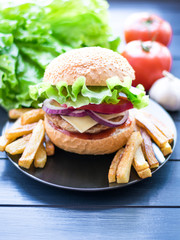Tasty fresh closeup burger and french fries on wooden table. Homemade hamburger with fresh vegetables.