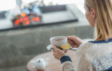 Woman seating next to fireplace drinking hot tea