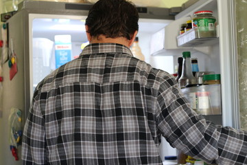 Fototapeta premium Rear View Of A Confused Young Man Looking At Food In Refrigerator