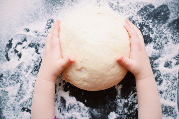Fototapeta premium Child's hands holding raw dough on wooden table.Process of baking, cooking.space for text.