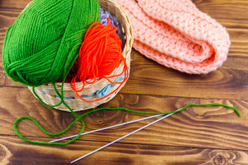 Wicker basket with colorful knitting yarns, knitting needles and knitted scarf on wooden table