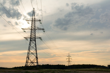two towers of high-voltage transmission lines stand on sunset background