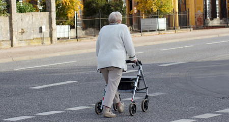 Alte Frau mit Rollator überquert die Straße